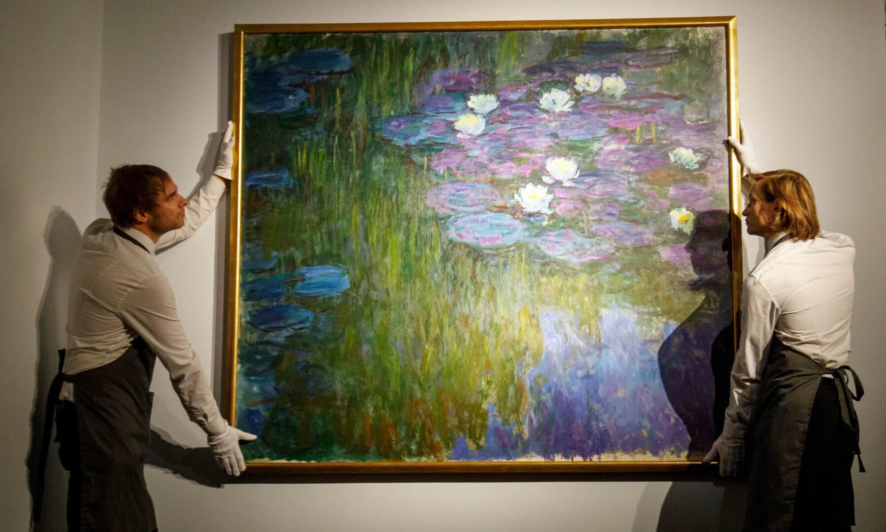 Two white-gloved art handlers carefully positioning Claude Monet’s Water Lilies painting against a gallery wall, symbolising private art collections, exclusive art sales, and high-value art auction events.