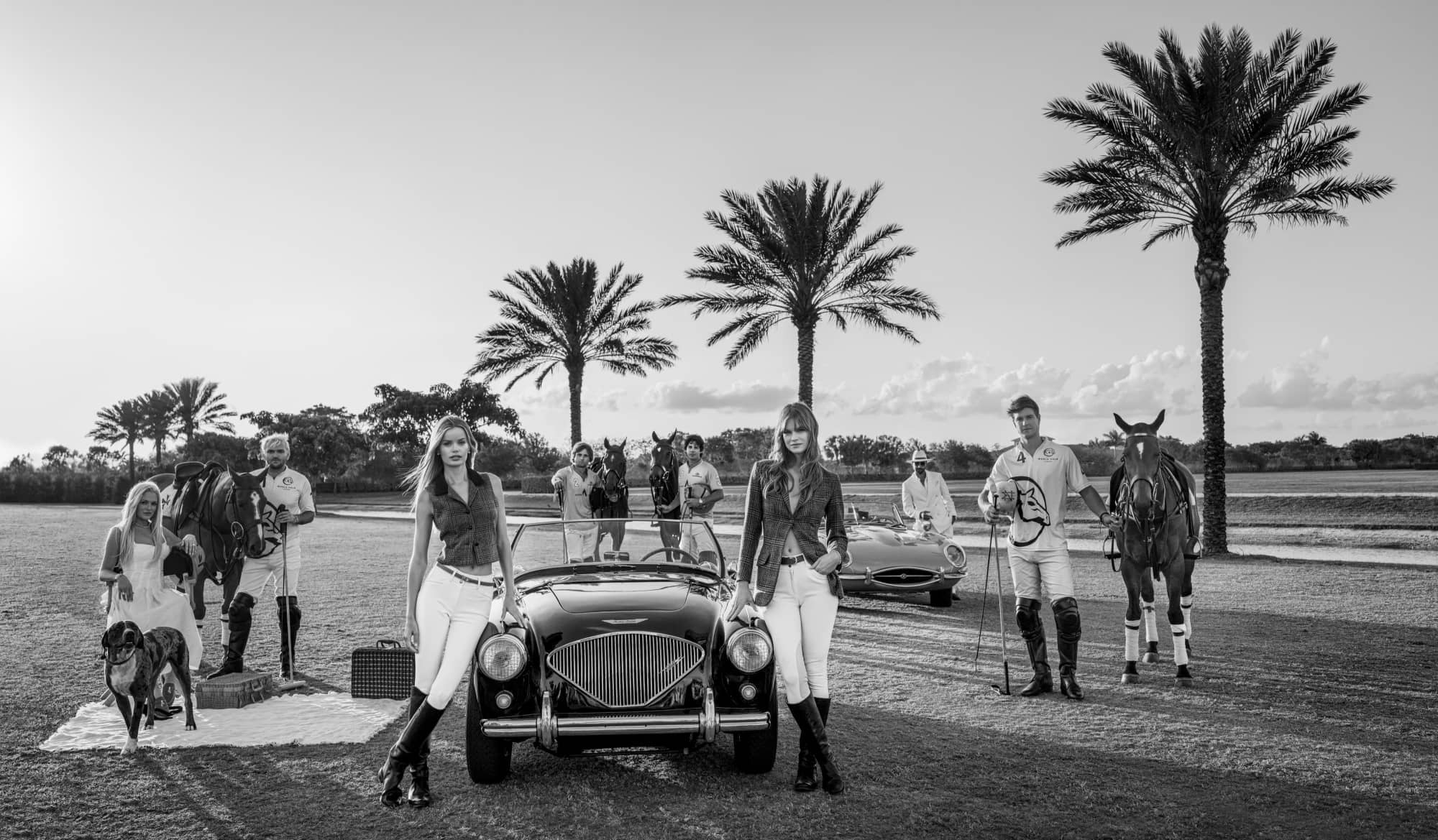Models, polo players, classic cars, horses, and dogs are posed under palm trees in a black-and-white David Yarrow photograph titled Players, evoking luxury and timeless Americana.