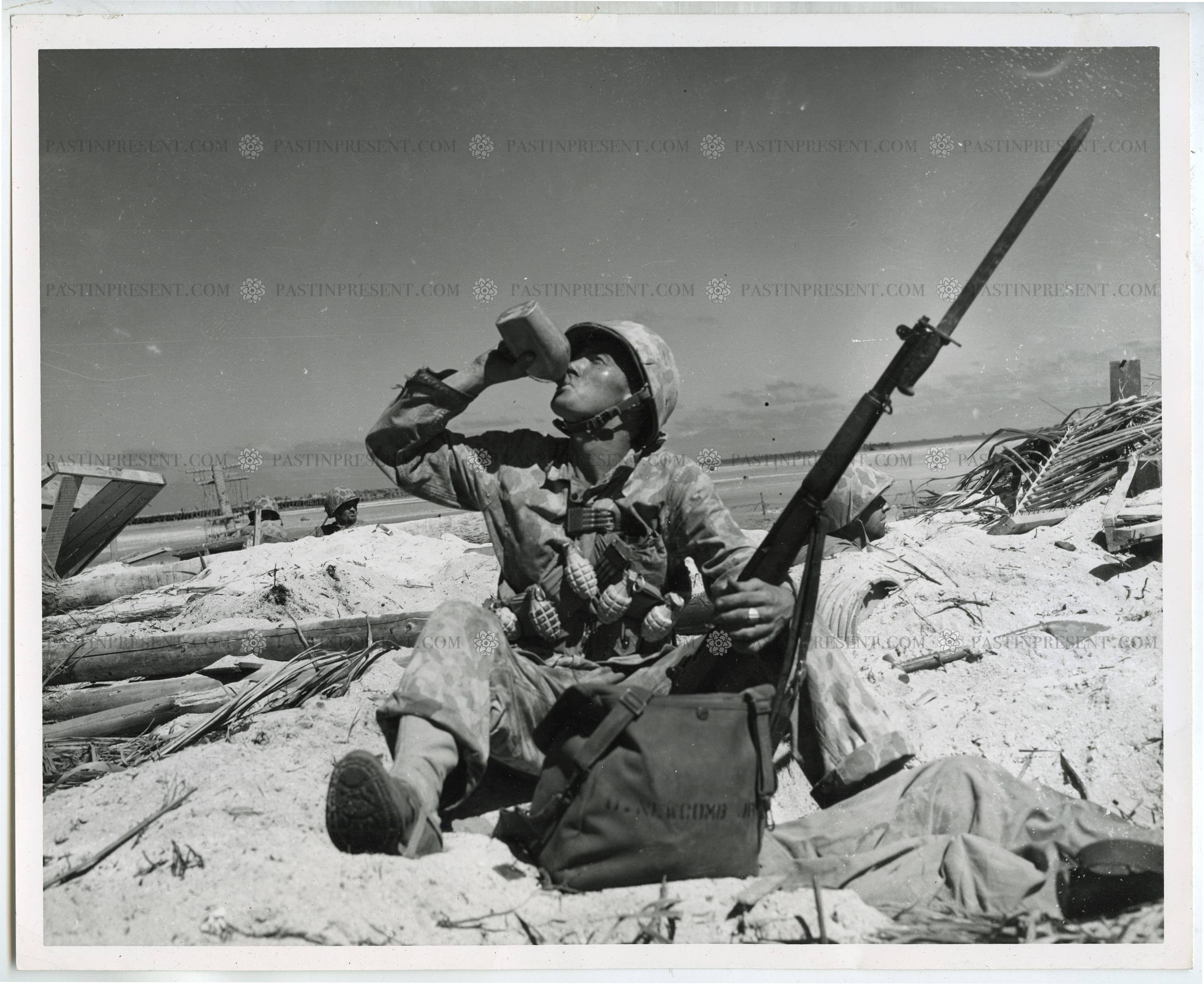 "Time Out" Marine draped with hand grenades and extra clip of ammunition takes time out for a drink from his...