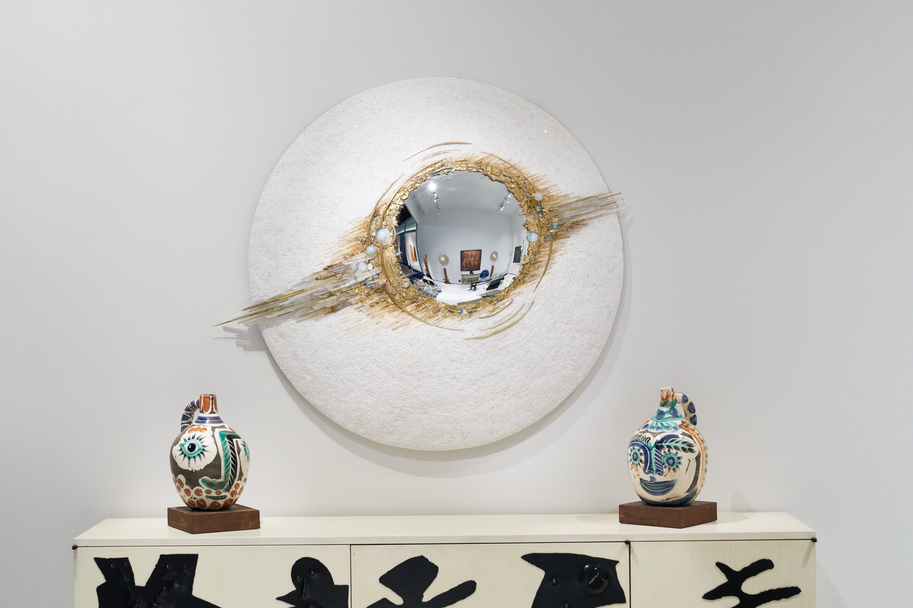 A spectacular witch mirror by Béatrice Serre is flanked by an imperfect pair of vases by Pablo Picasso.