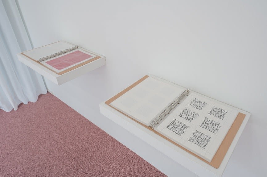 さらに、プロジェクトには《RGB-1》《RGB-2》という二冊の書籍が存在します。《RGB-1》はジャオが制作した赤い石のすべての色情報をデータ化したものであり、《RGB-2》は現地の人々が制作した本来のマニ石の色彩データを収録しています。いずれも石の表面の赤色を精密機器で測定し、摘出されたRGB値の数字を、ゴム印によって一つずつ手押しで印刷したもので、極めて繊細な作業によって構成されています。本展示では、その二冊が展示棚の上に開かれた状態で置かれており、観客の方々は自由にページを閲覧することができます。また、これらの書籍から派生した7.5cm角の印刷紙は、ピラミデビル内の展示空間の床にも散りばめられています。各データをカラーコード変換システムなどに読み込ませると、微妙に異なる“赤”として再現され、日常の繰り返しのなかに潜むわずかな差異の感覚を想起させます。書籍の最終ページに印刷されている「精臻紅(ジンジェンホン)」は、日本ペイント社が“チベットへの印象”をもとに開発した人工の赤色です。中国語における「精臻」とは、「精神を集中させる」「厳選する」という意味を持ち、この作品全体の象徴的な色として用いられています。