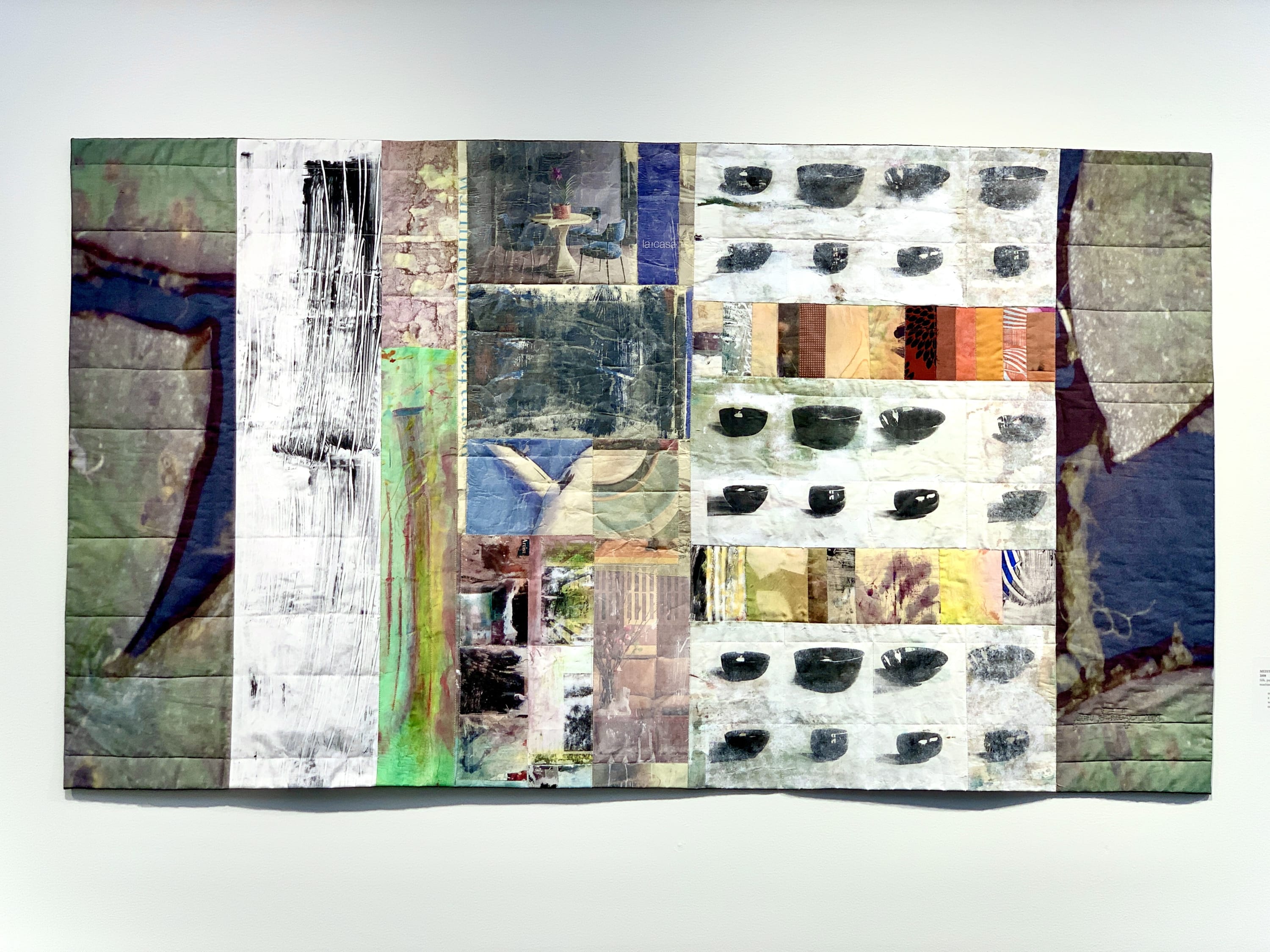 This rectangular quilt is composed of varied rectangular panels, some stretching the full height of the quilt, some much smaller. The larger panels are darker grey-green and seem to contain close up photographic transfers of patterns - perhaps from the su