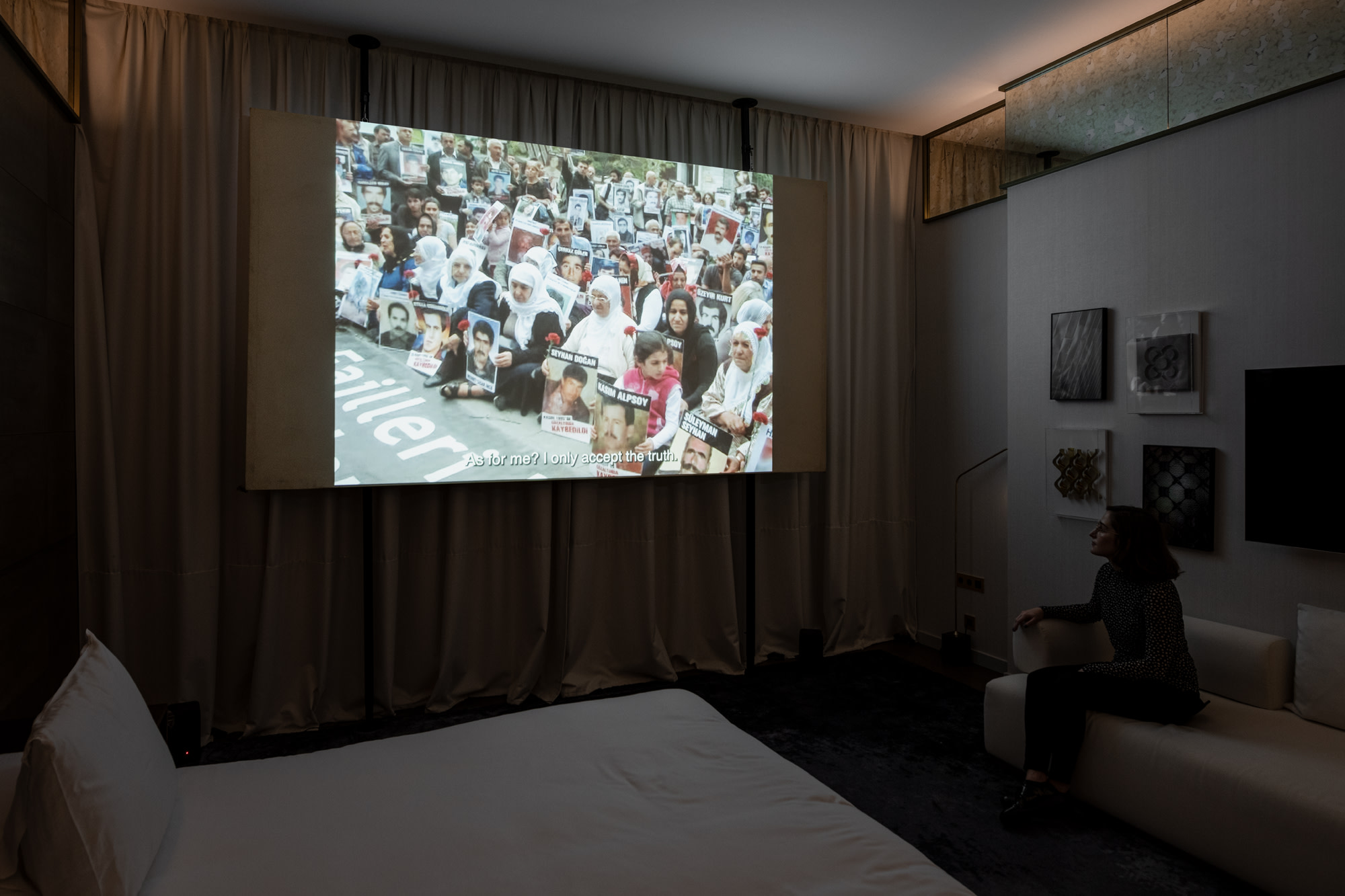 a video projected on a screen in a hotel room with a woman watching from a sofa