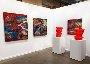 Installation view at the Dallas Art Fair with several colorful knitted works by Channing Hansen and two red pots on plinths by Beverly Semmes