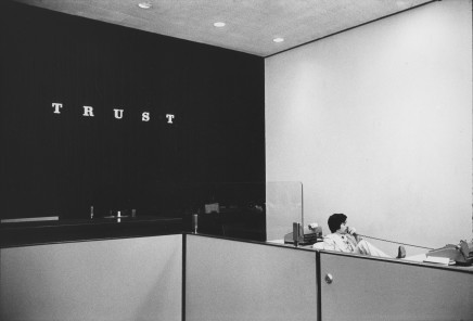 Jill Freedman, Untitled [Man on phone with “Trust” on office wall], circa 1976