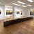 Installation view of Yoan Capote's exhibition in a white walled gallery featuring black and gold paintings and a long low black stone sculpture