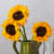 Detail of painting of three sunflowers in a green pitcher. The center of the sunflowers have dog faces in them.