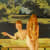 nude girl seated on top of a picnic table next two another nude girl sitting on an accompanying bench