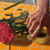 Painting on a hand resting on a small cup with freshly cut flowers on a bright orange tablecloth