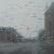 An out of focus view of a road with buildings on either side through a window covered in water droplets by artist Esther Nienhuis.