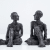 Two individual Carol Peace sculptures, a man and a woman, seated with their legs crossed mirroring each other, they look conversation. Highly textured and the iron resin is almost black.