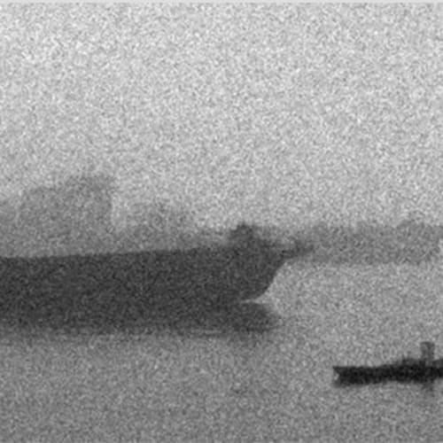 A few cargo ships are parked on the river surrounded by fog