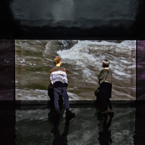 There are two viewers standing in front of the interior projection of landscape