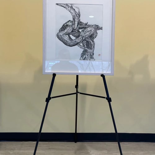 an artwork with black cirrus depicted on a piece of white paper, exhibiting on a tripod stand