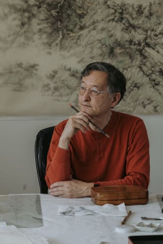 Arnold Chang sitting in his studio with a brush in his hand