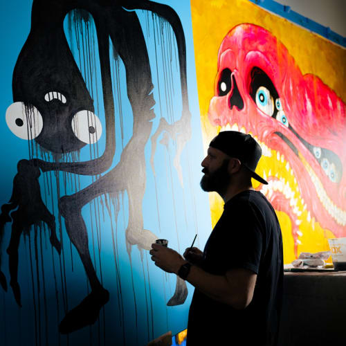 portrait of artist Alex Pardee facing two canvases
