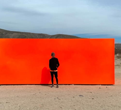 photograph of Artist Huntz Liu standing in front of a red wall