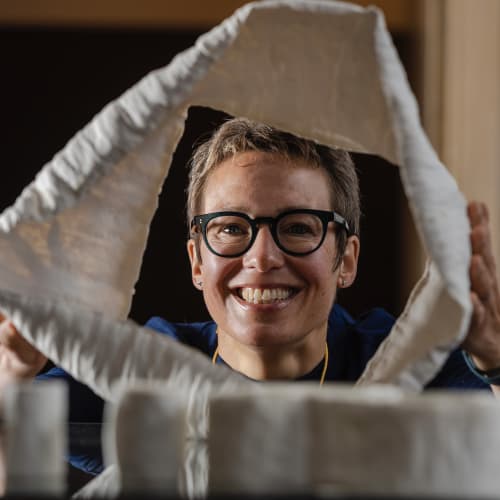 A person smiling through a geometric sculpture made of textured white material, photographed indoors.