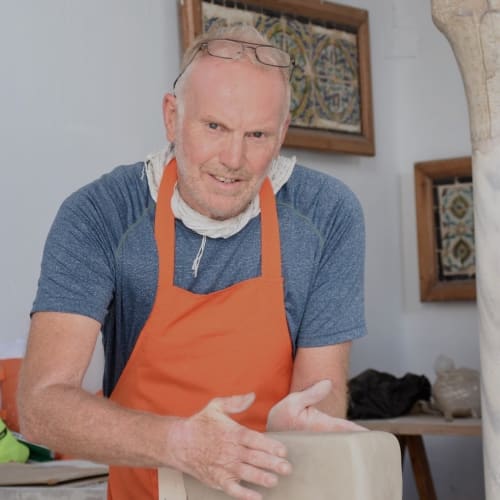 Man in an orange apron working with clay in a studio setting.