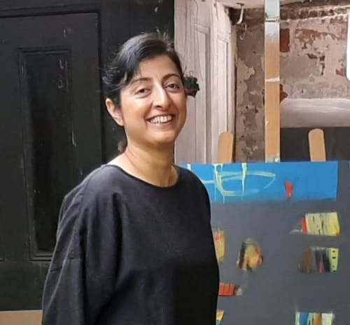Person standing and smiling in front of a partially visible abstract painting on an easel.