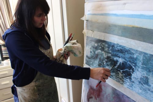 Nerine Tassie painting ocean-themed artwork on large canvas in studio.