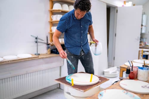 Artist Adam Frew working in his studio, surrounded by pottery tools and ceramics.