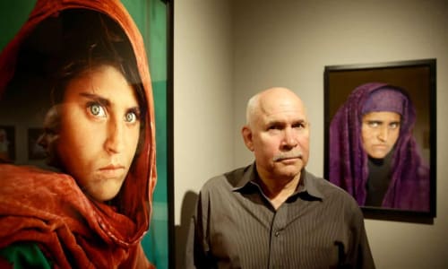 Steve McCurry next to Afghan Girl, with his portrait of Sharbat Gula, taken nearly two decades later, in the background. Photograph: Ulrich Perrey/AFP