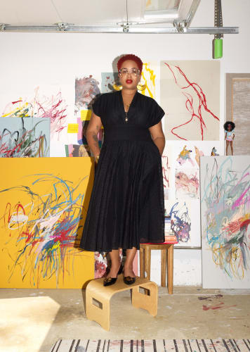 © A’Driane Nieves, with various examples of her work, wears a Tory Burch dress and shoes; her own glasses and jewelry. Photograph by Frederike Helwig