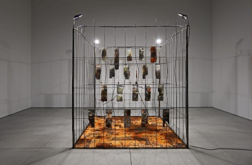 Marcin Dudek, Sektor, 2021, Steel fence, jesmonite, ash, resin, textile, medical tape, acrylic paint, image transfer, wood, uv varnish, flood lights. 240 x 210 x 210 cm - 94 1/2 x 82 5/8 x 82 5/8 in. Courtesy of Galerie Ron Mandos and Harlan Levey Projects