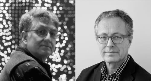 A black-and-white portrait image featuring two men side-by-side. On the left is a man with short, wavy hair and glasses, wearing a patterned shirt and a vest. He is facing the camera with a thoughtful expression against a blurred background of circular li