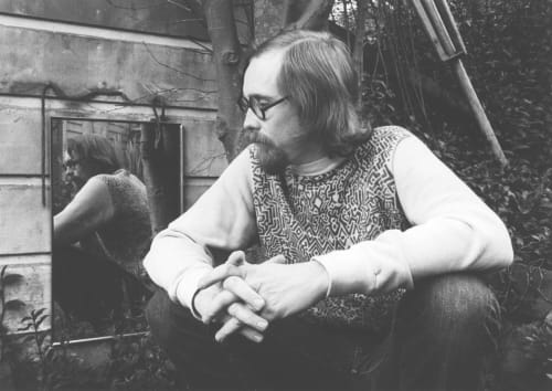 Man waering a custom best oin a black and white image sitting in from of a mirror with long hair