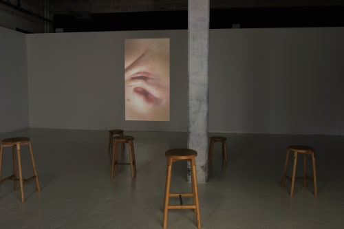 Dark theatre with wooden stools and projection of Piccinini's The Awakening.