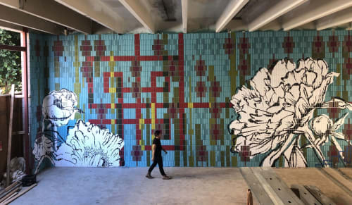 Person walking by large mural in blues red and greens with very large black and white peony designs overlaid on top of mural designs