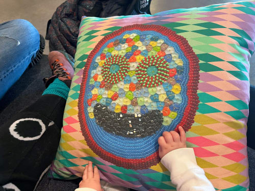 Author’s daughter with pillow from Jeffrey Gibson, I AM YOU RELATIVE (2022). Detail view, MOCA Toronto. Co-commission by MOCA and the Toronto Biennial of Art (2022) (courtesy Jeffrey Gibson Studio, All photos Rea McNamara/Hyperallergic)