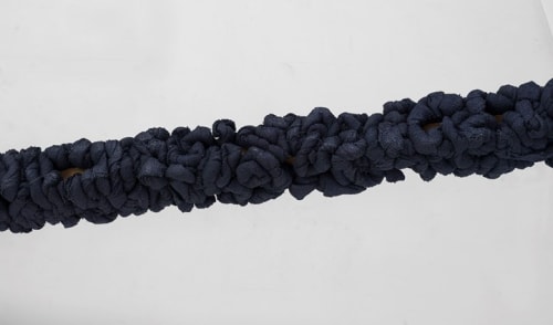 Manish Nai’s Untitled (2017): five large sticks wrapped in compressed strips of burlap dyed indigo leaning upright against a wall.