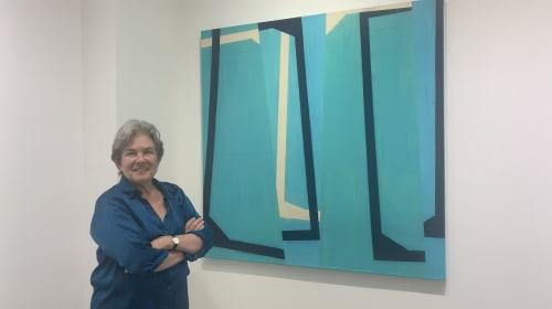 Woman with arms crossed standing next to an abstract blue and white painting