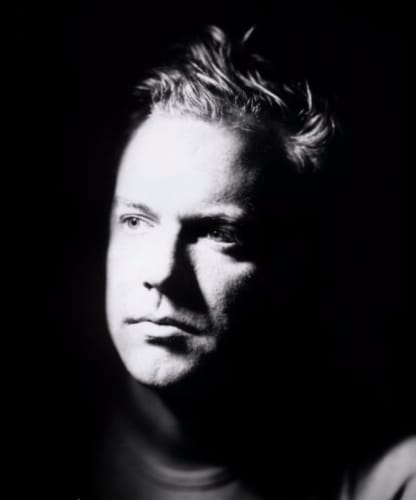 Marco Walker artist photo, he sits in a 3/4 profile position with half of his face illuminated by a key light, looking off frame. Image is grayscale.