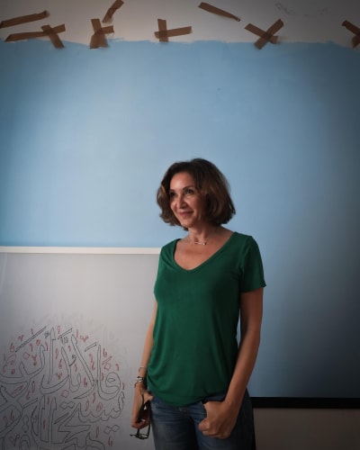 Tunisian visual artist Hela Ammar standing next to an artwork, with a blue background