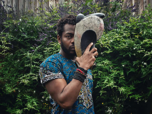 Nigerian visual artist Asiko holding a shell standing in front of a garden