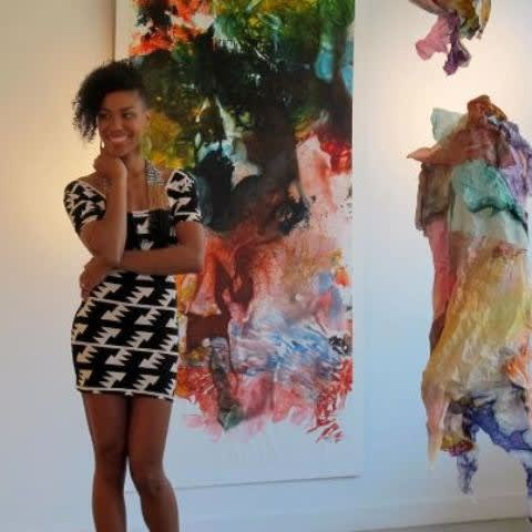 Artist Maya Freelon wearing a dress, standing in front of her artwork