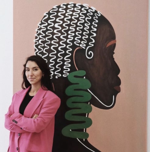 Mafalda Vasconcelos in front of her work representing a portrait of an African woman on a bright pink pastel background.
