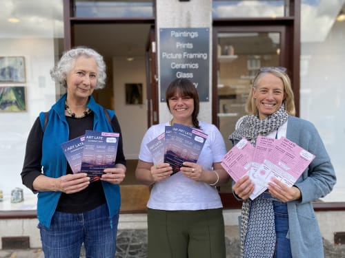 Three women stand outside Sarah Wiseman Gallery, holding up flyers advertising Art Late Summertown