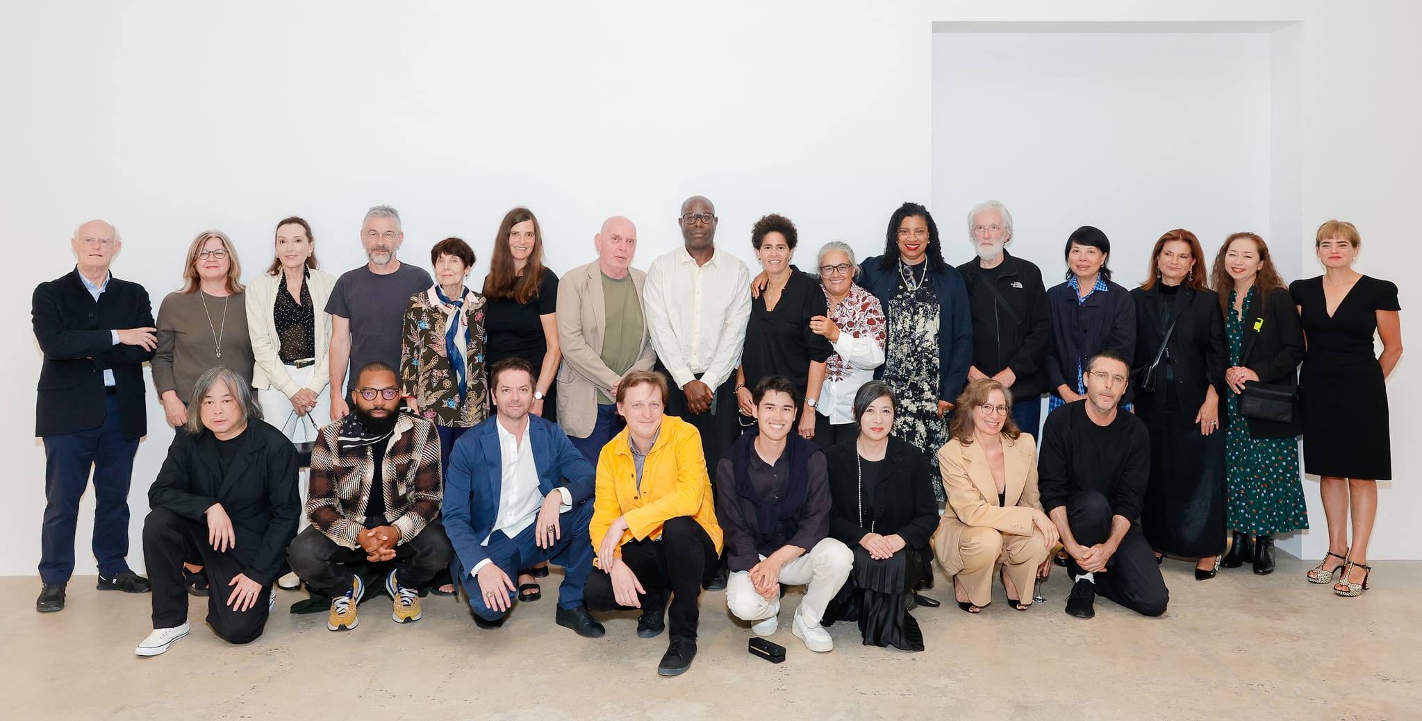 A large group of artists at Marian Goodman Gallery, LA, posing for the camera in front of a white wall. 