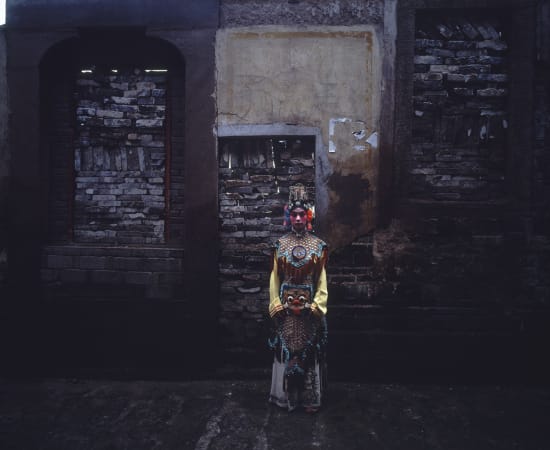 Artist Chen Qiulin dressing the traditional opera costumes stands in front of a wall. 
