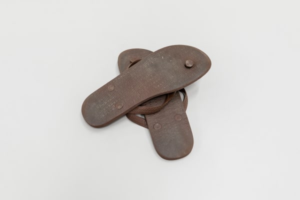 Ana Raylander Superstição, 2023 Par de chinelos usados, cruzados e virados de cabeça para baixo. Numeração 41. 42 x 29 cm (sem moldura)