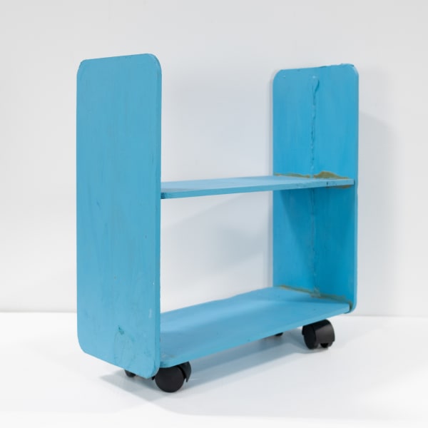 A small, teal, wooden U-shaped Sculpture with a board in the center on casters.