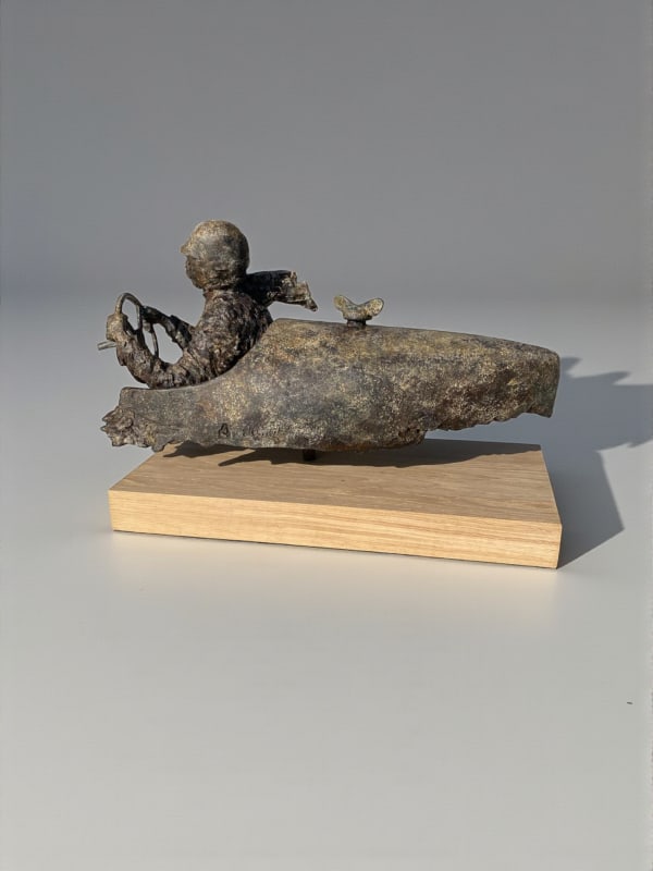 Sculpture en bronze “Master of Speed V” de Lieven D’Haese, représentant un personnage assis dans un véhicule stylisé avec un petit oiseau posé à l’avant.