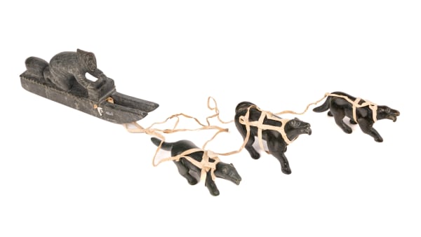 Lot 9 DANIEL OWEETALUKTUK (1934-D?) INUKJUAK (PORT HARRISON) Man on Qamutiik (Komatik) with Three Sled Dogs, c. 1960s stone and leather, dimensions variable, the hunter on sled: 3 x 8.5 x 1.25 in (7.6 x 21.6 x 3.2 cm) / the dogs, each, approx.: 1.5 x 4.5 x 1.25 in (3.8 x 11.4 x 3.2 cm) ESTIMATE: $300 — $500 PRICE REALIZED: $610.00