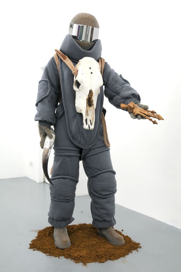 The Offering, 2012 Felt bomb disposal suit, flocked helmet, gloves and boots, fossilised bear claw, bull's horn, bull riding rope and sand 194 x 106 x 100 cm