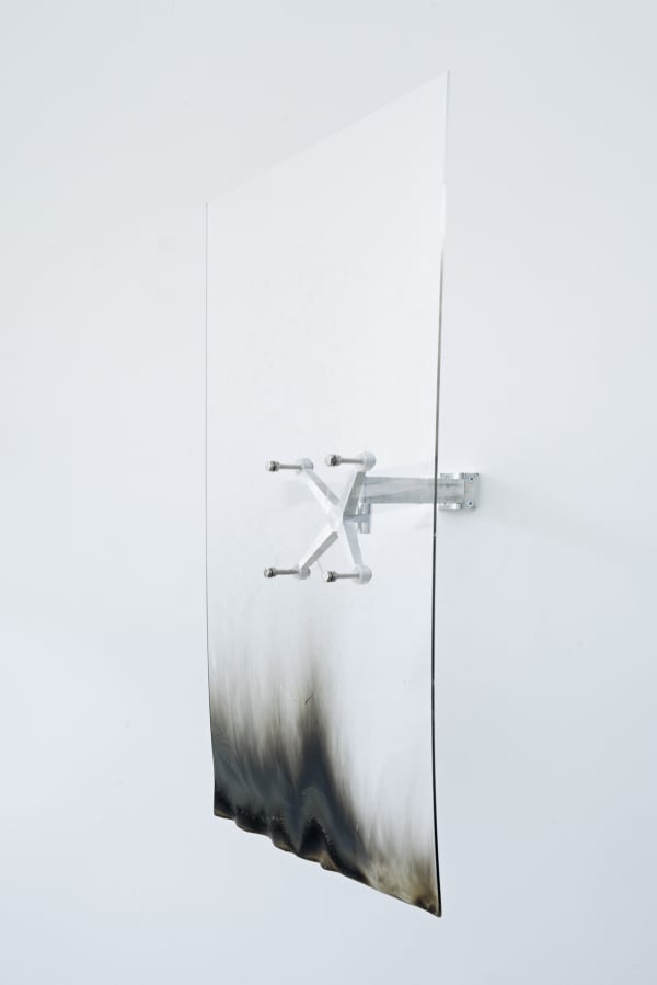 An image of a burned acrylic sheet attached to an aluminum spider arm against a white wall.